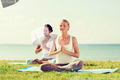 Image of smiling couple making yoga exercises outdoors