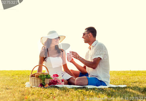 Image of smiling couple with small red gift box on picnic