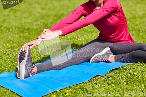 Image of close up of woman stretching leg on mat outdoors