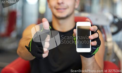 Image of young man with smartphone showing thumbs up in gym