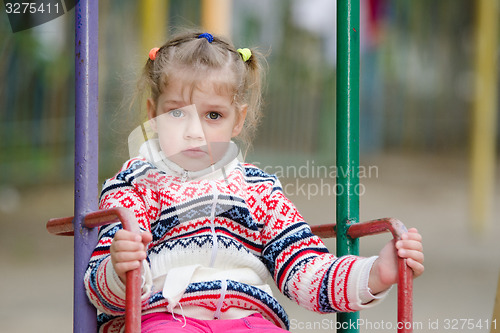 Image of Upset four-year girl riding on a swing