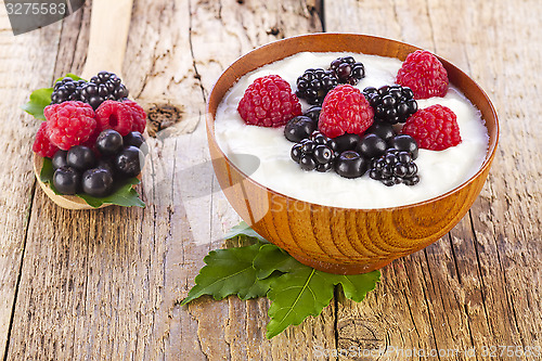 Image of yogurt with wild berries in wooden bowl on wooden 