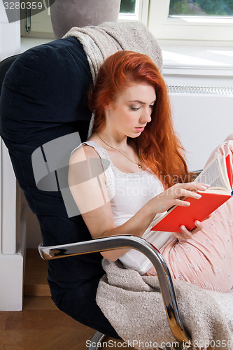 Image of Young Woman Sitting on Chair While Reading a Book