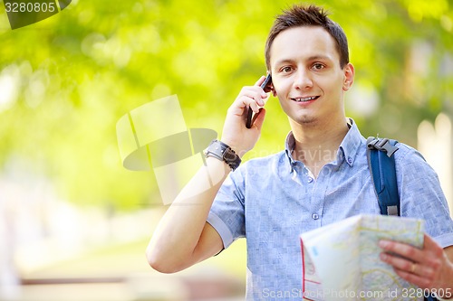 Image of Man holding map outdoors and talking by phone