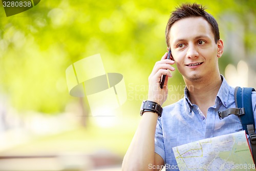 Image of Man holding map outdoors and talking by phone