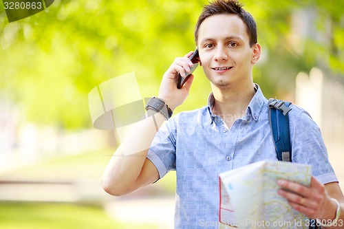 Image of Man holding map outdoors and talking by phone