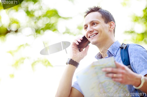 Image of Man holding map outdoors and talking by phone