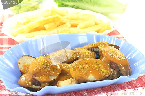 Image of Currywurst with french fries on a checkered napkin