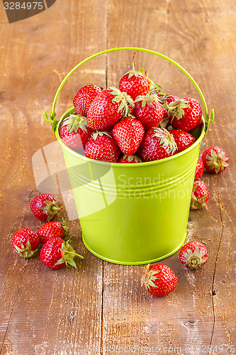 Image of strawberry in a green metal bucket on wooden 