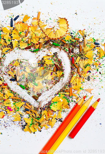 Image of heart, three pencils and varicolored wooden shavings