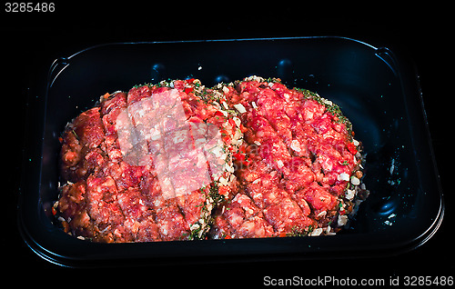 Image of Two raw red burgers in a black plastic tray isolated on black