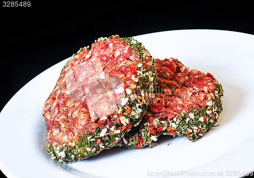 Image of Closeup of raw red hamburgers on white plate isolated on black