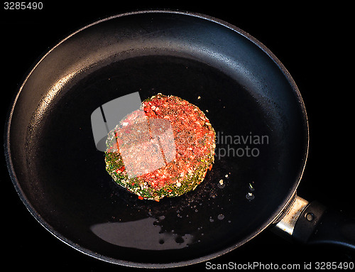 Image of Raw red seasoned hamburger in fry pan isolated on black