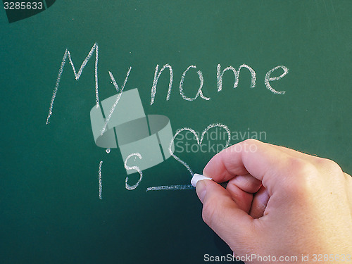 Image of Person writing on green chalkboard with calk