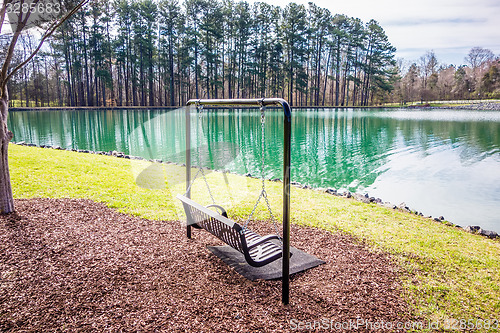 Image of Empty wooden park bench overlooking a lake or pond