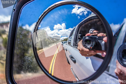 Image of  camera reflected in the rearview mirror of a car on a summer da