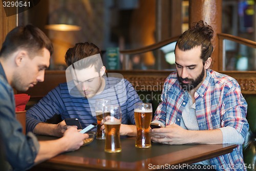 Image of male friends with smartphones drinking beer at bar