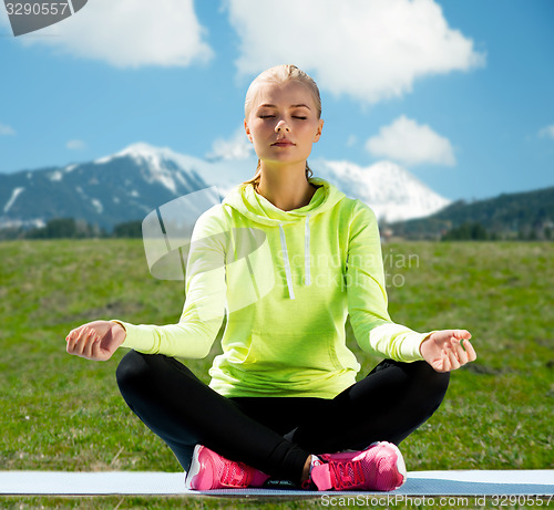 Image of woman sitting in lotus pose doing yoga outdoors