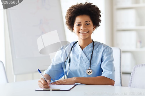 Image of happy female doctor or nurse writing to clipboard