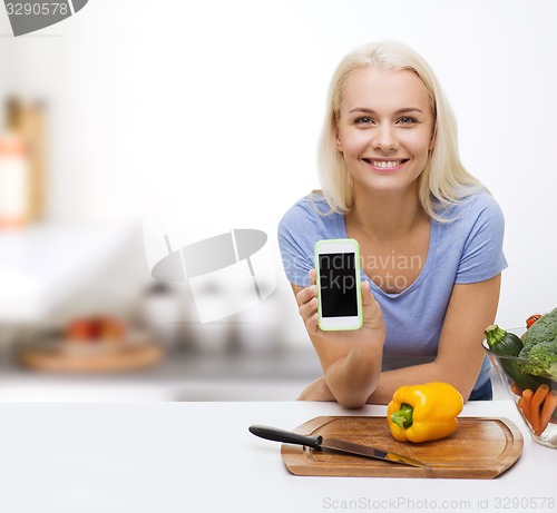 Image of smiling woman with smartphone cooking vegetables