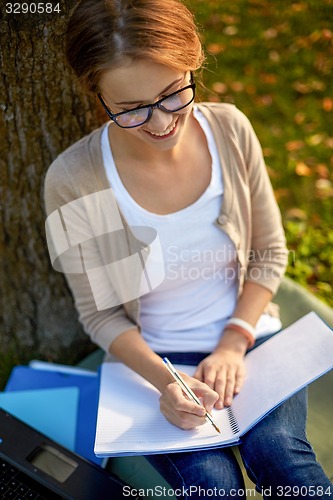 Image of happy student girl writing to notebook at campus