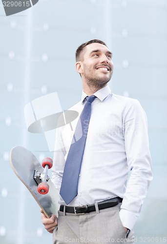 Image of young smiling businessman with skateboard outdoors
