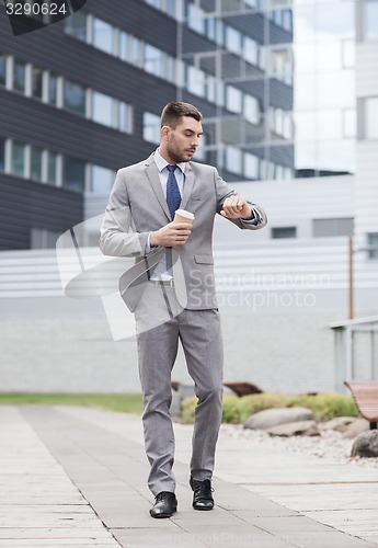 Image of young serious businessman with paper cup outdoors