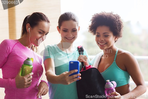 Image of happy women with bottles and smartphone in gym