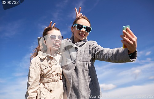 Image of happy girls with smartphone taking selfie outdoors