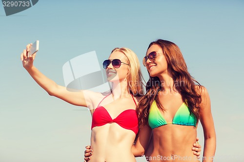 Image of two smiling women making selfie on beach