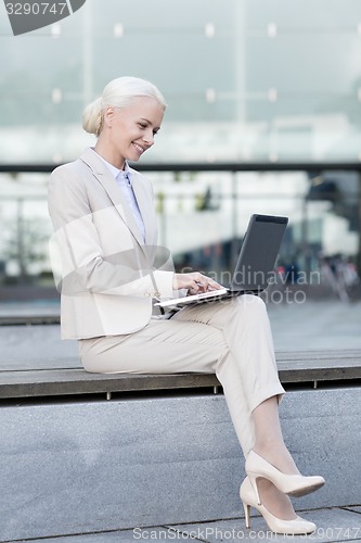 Image of smiling businesswoman working with laptop outdoors