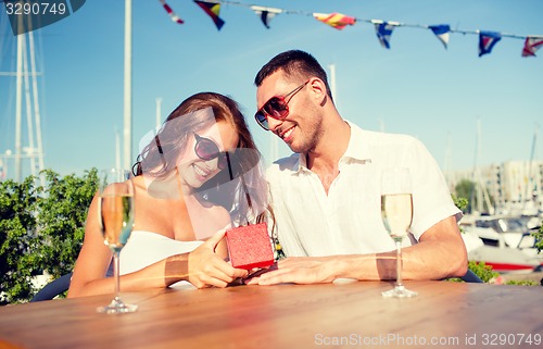 Image of smiling couple with champagne and gift at cafe
