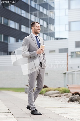 Image of young serious businessman with paper cup outdoors