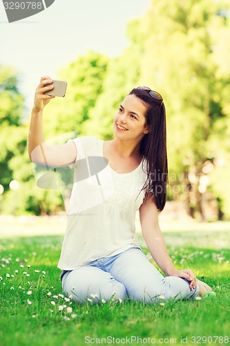 Image of smiling young girl with smartphone sitting in park