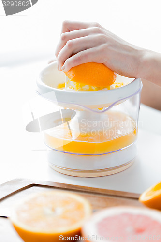 Image of woman with squeezer squeezing orange juice at home