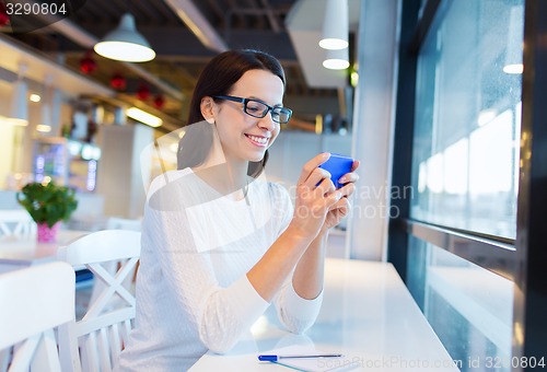 Image of smiling woman with smartphone at cafe