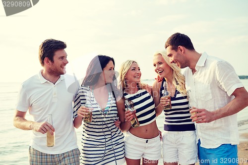 Image of smiling friends with drinks in bottles on beach