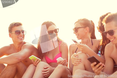 Image of group of smiling friends with smartphones on beach