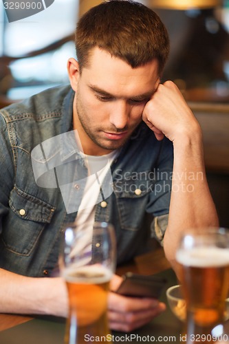 Image of man with smartphone and beer texting at bar