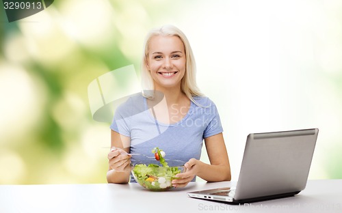 Image of smiling woman eating salad with laptop
