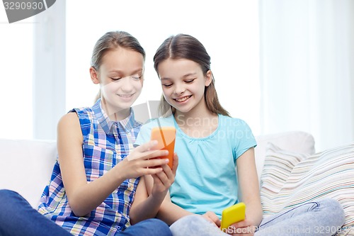 Image of happy girls with smartphones sitting on sofa