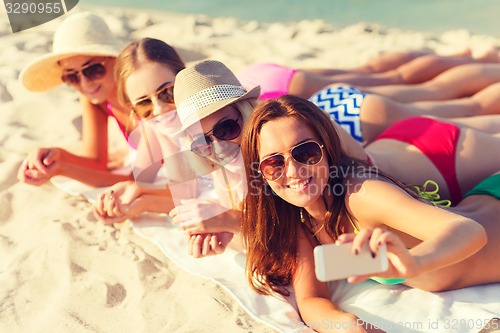Image of group of smiling women with smartphone on beach