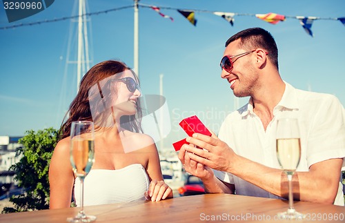 Image of smiling couple with champagne and gift at cafe