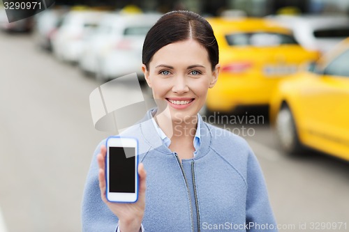 Image of smiling woman showing smartphone over taxi in city