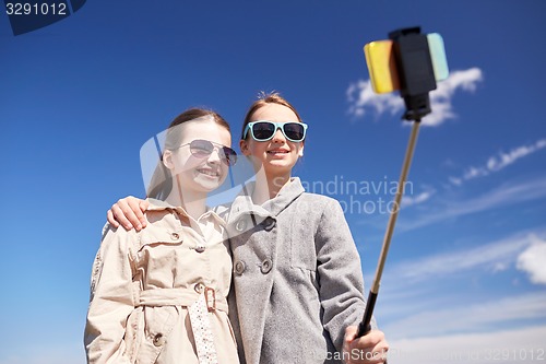 Image of happy girls with smartphone selfie stick