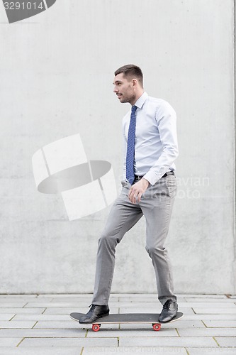 Image of young smiling businessman with skateboard outdoors