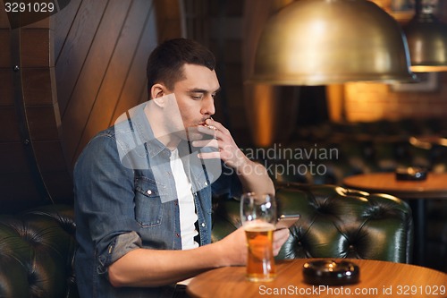 Image of man drinking beer and smoking cigarette at bar