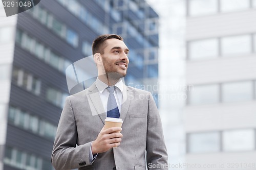 Image of young smiling businessman with paper cup outdoors