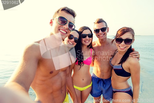 Image of group of smiling friends making selfie on beach