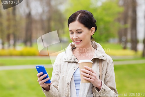 Image of smiling woman with smartphone and coffee in park